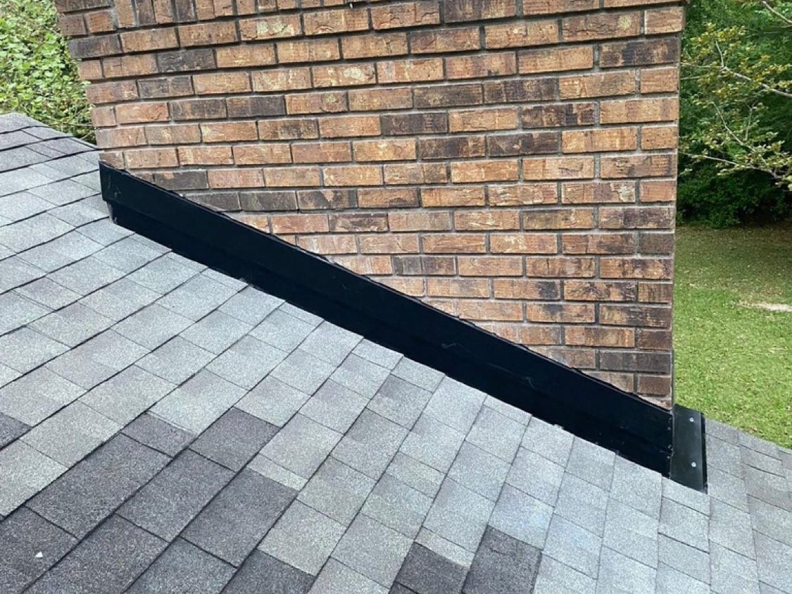 New black step flashing sealed against a brick chimney on a grey architectural shingle roof in Gulfport Mississippi