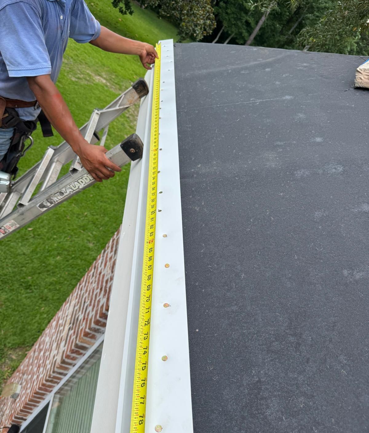 A hand holding a tape measure along the new drip edge on the Biloxi roof to document fastener spacing