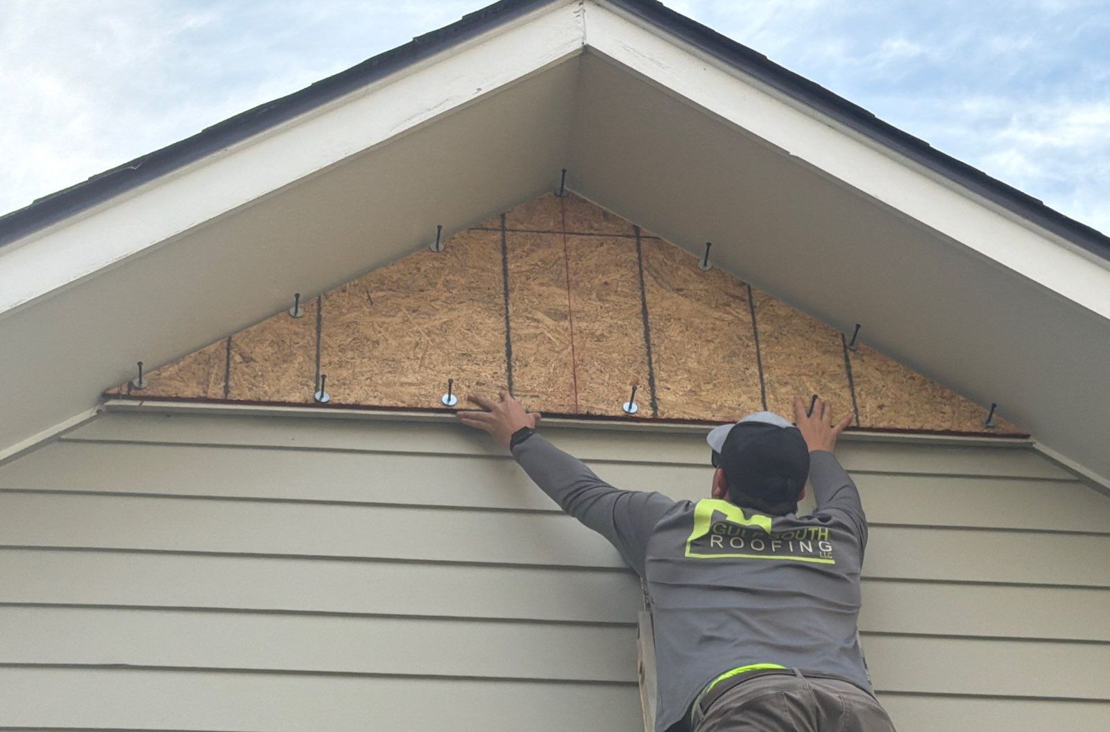 A crew member fitting a cut plywood storm cover over the gable louver of the Gulfport home for the FORTIFIED evaluator