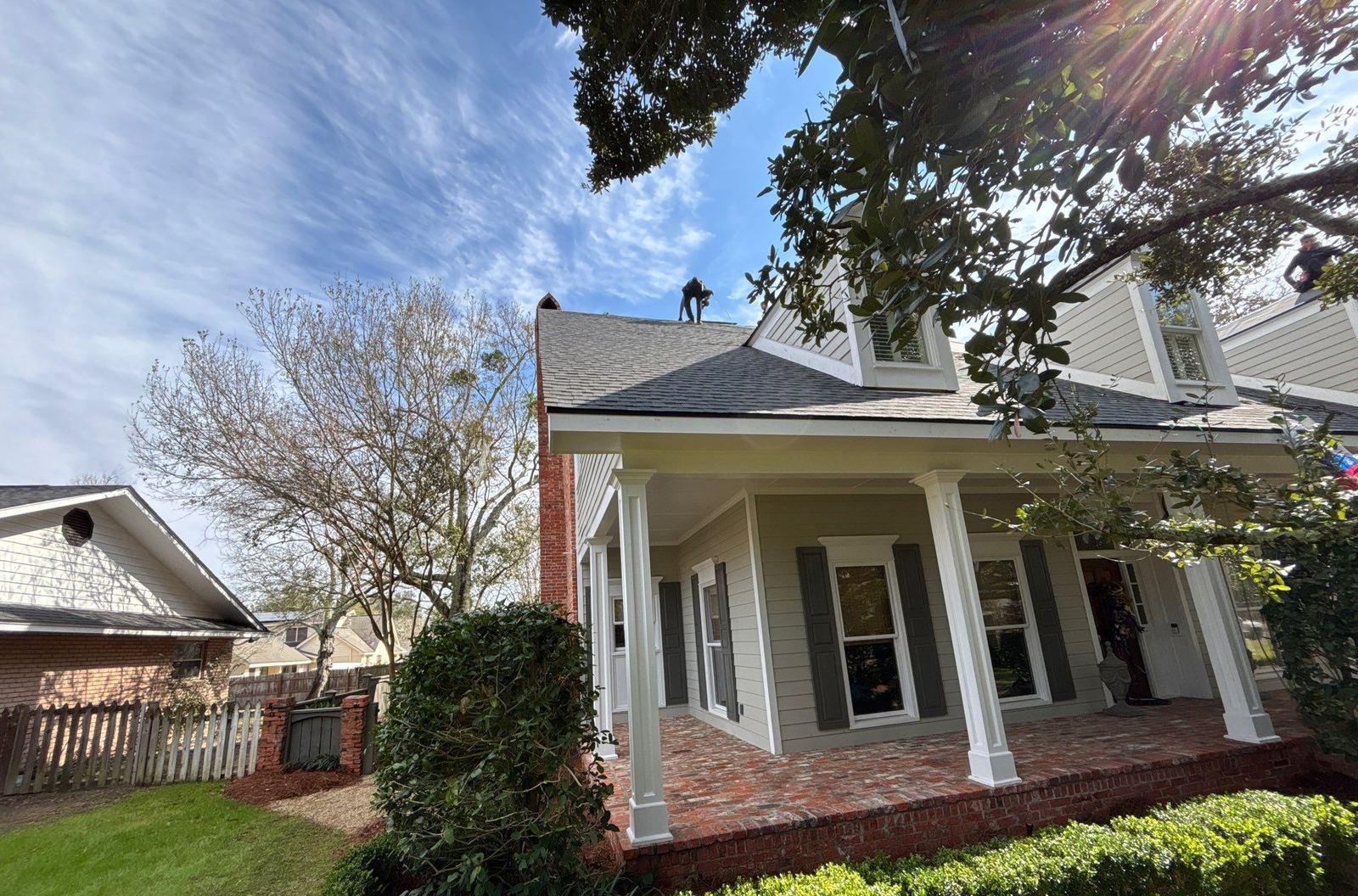 Front porch and dormer of the Gulfport home with the new roof on and a crew member finishing the ridge