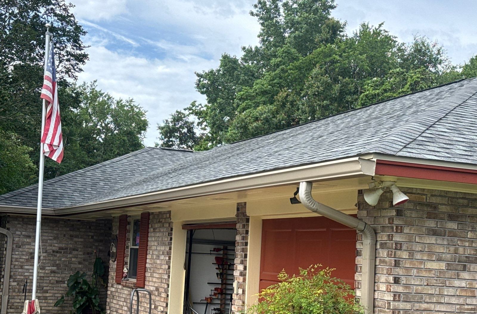 Front of the brick Long Beach home under its completed FORTIFIED Colonial Slate shingle roof, flag up and red garage doors