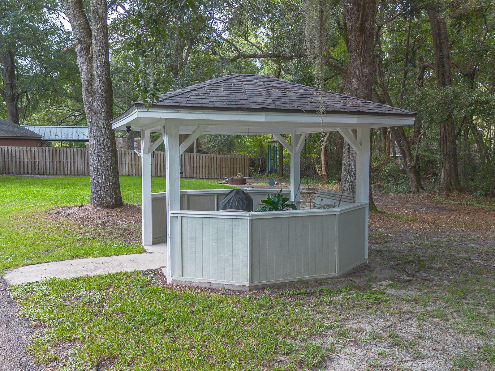 Backyard gazebo under live oaks with its small hip roof re-shingled to match the house