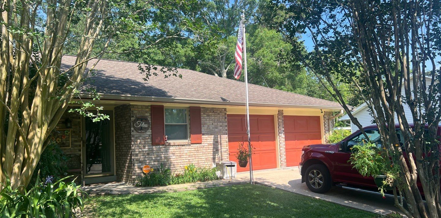 Front of the brick Long Beach home with its worn brown shingle roof before the FORTIFIED replacement, flag and red garage doors