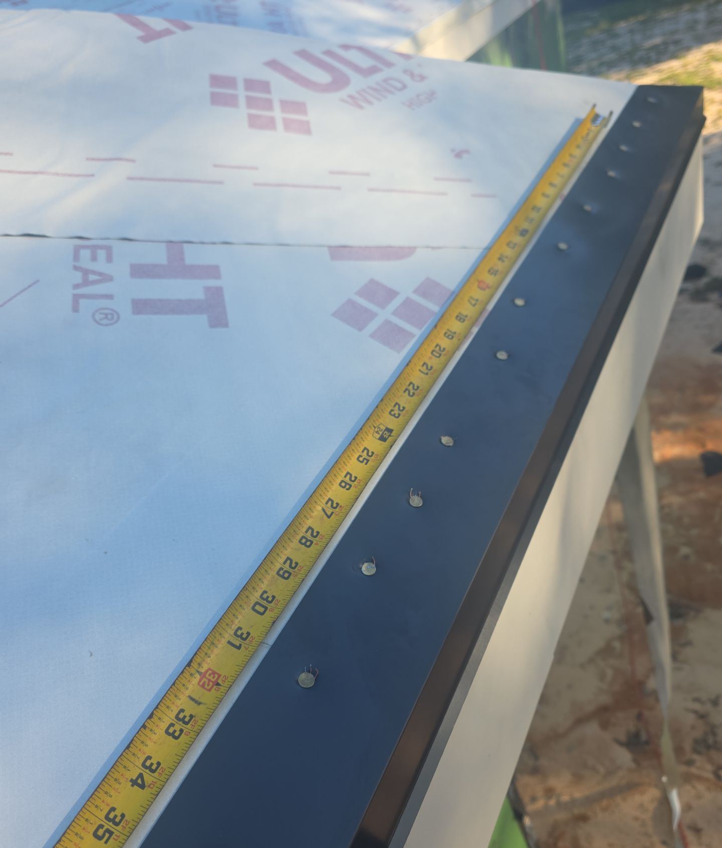 High-temperature self-adhering underlayment and black drip edge on the new roof deck, with a tape measure at the eave