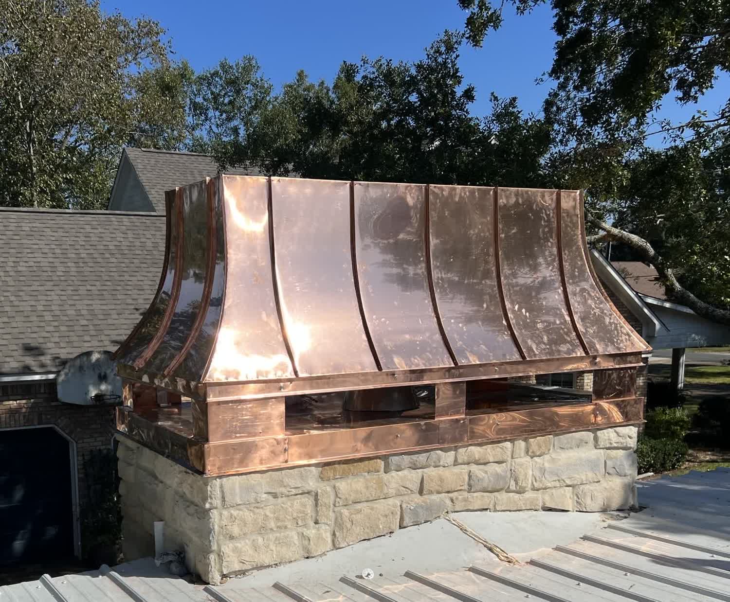 Hand-formed copper chimney hood fabricated by Gulf South Roofing, installed on a stone chimney on the Mississippi Gulf Coast