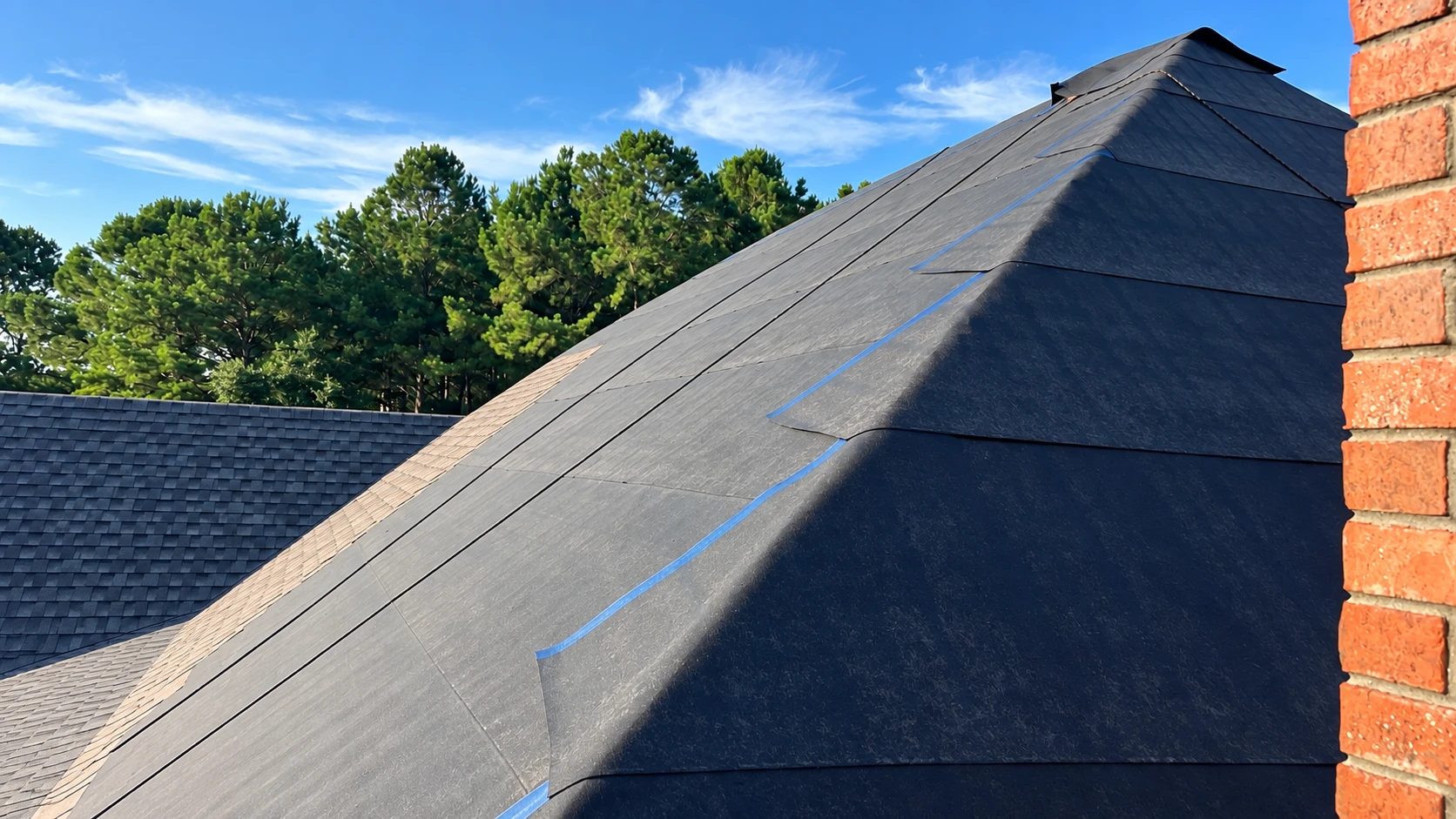 A roof deck fully sealed with self-adhering ice-and-water membrane, every seam lapped and taped, beside a brick chimney on a Gulf Coast home