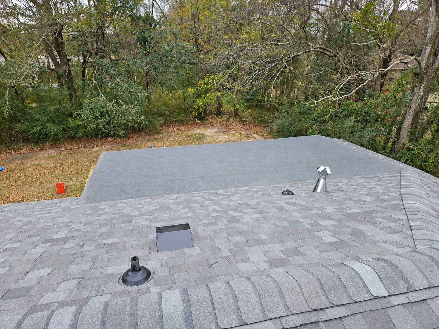 A modified bitumen membrane on the low-slope section of a Gulf Coast home, meeting the shingle field with new pipe boots