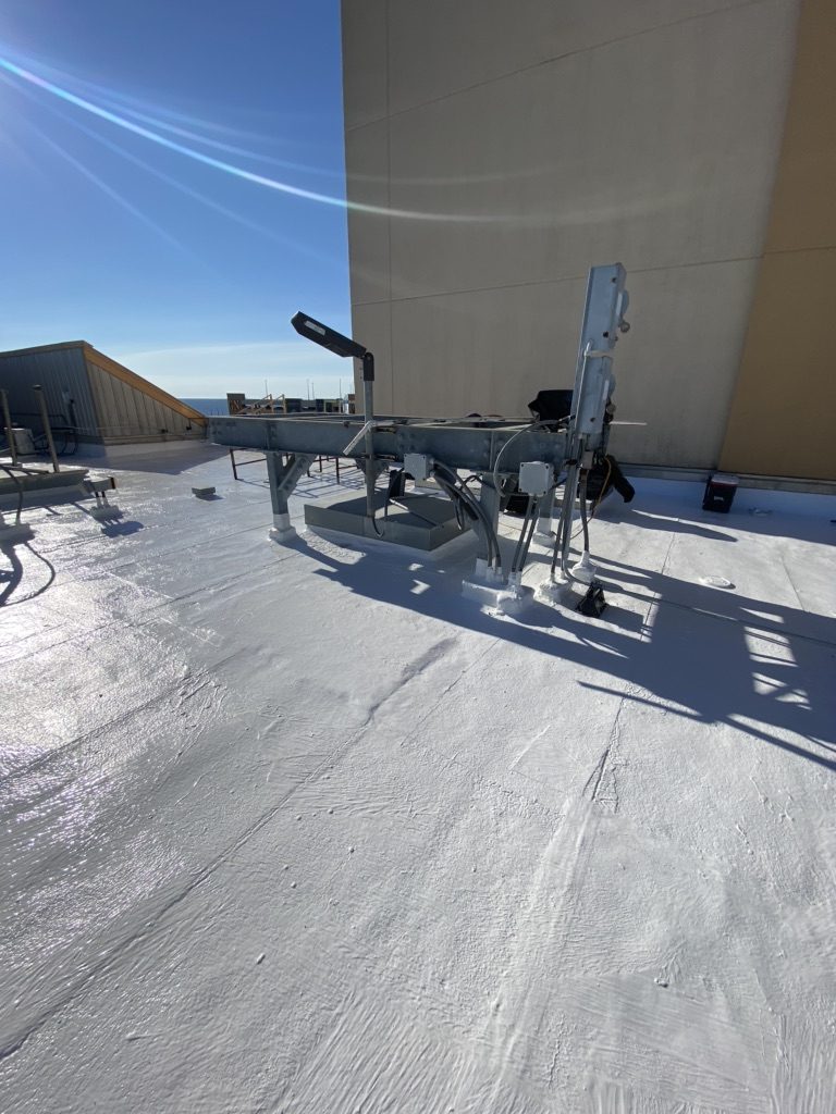 A white silicone restoration coating over a commercial flat roof, rooftop equipment curbs sealed in, on the Mississippi Gulf Coast
