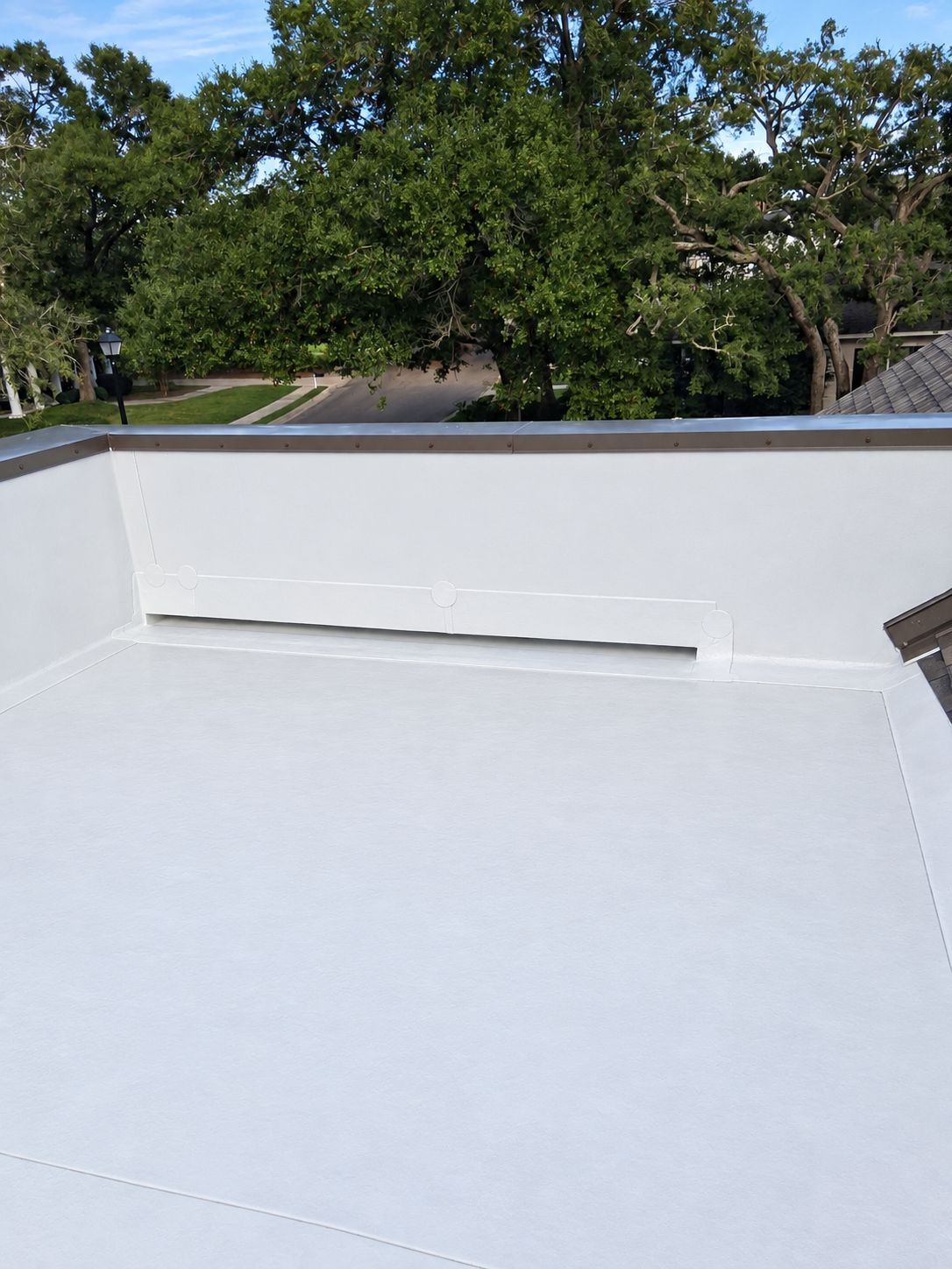 A finished white TPO membrane on a residential low-slope deck, edges and parapet detailed by the same crew